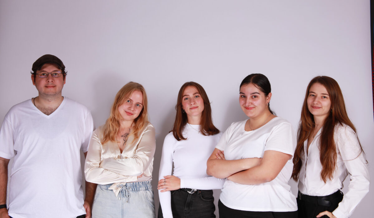 Das junge Journalismus-Team steht nebeneinander vor einem hellen Background.